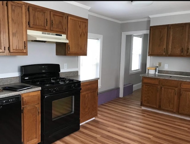 kitchen with brown cabinets, crown molding, light wood-type flooring, under cabinet range hood, and black appliances