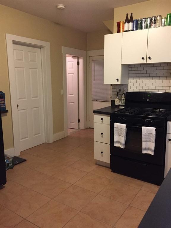 kitchen featuring light tile patterned floors, tasteful backsplash, dark countertops, black range with gas stovetop, and white cabinetry