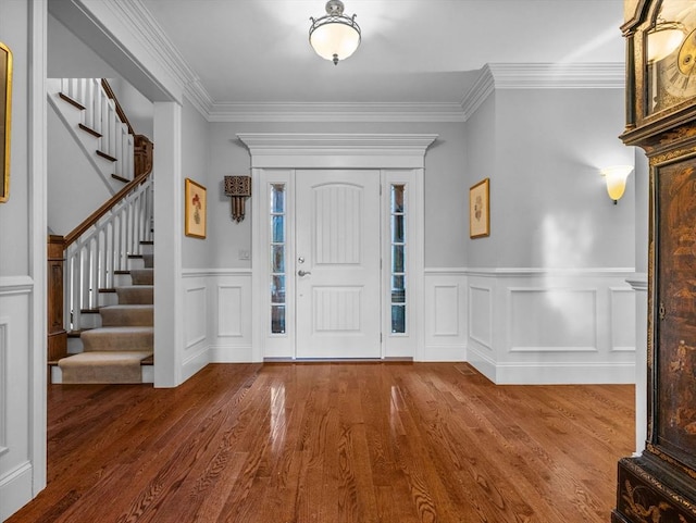 entrance foyer featuring stairs, crown molding, a decorative wall, and wood finished floors