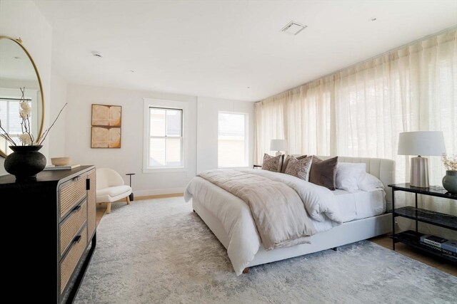bedroom featuring baseboards, visible vents, multiple windows, and wood finished floors