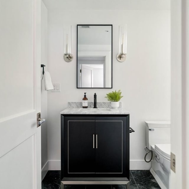 half bath with baseboards, vanity, and toilet