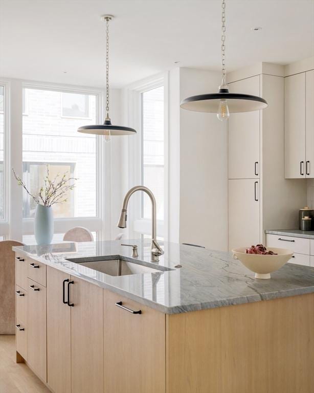 kitchen with light stone counters, a sink, modern cabinets, and a healthy amount of sunlight
