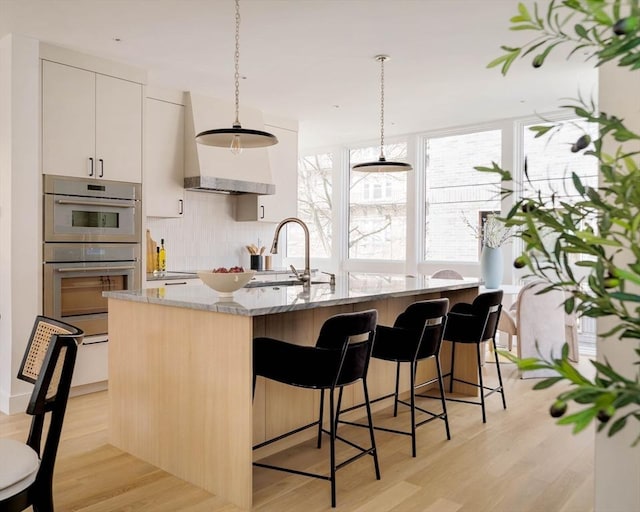 kitchen with a sink, light stone countertops, stainless steel double oven, and light wood finished floors