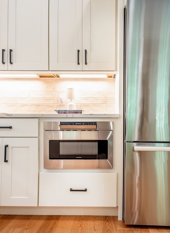 kitchen with light hardwood / wood-style floors, tasteful backsplash, white cabinetry, and appliances with stainless steel finishes