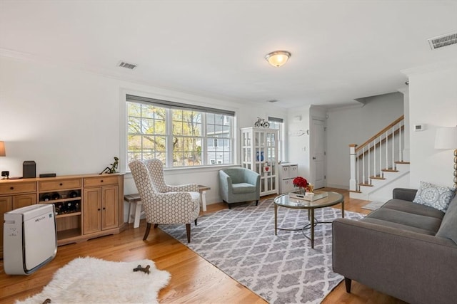 living room with crown molding, light wood finished floors, and visible vents