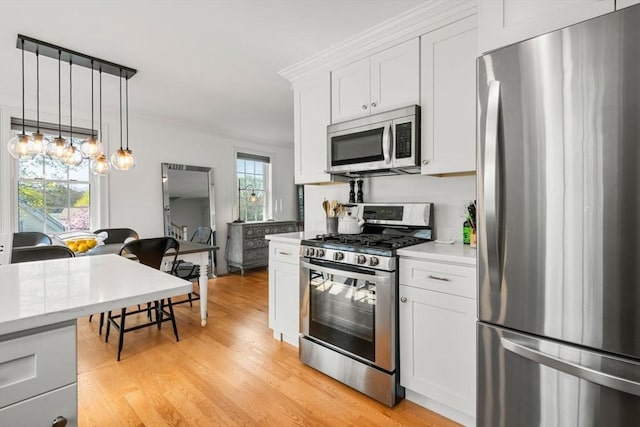 kitchen featuring decorative light fixtures, appliances with stainless steel finishes, light countertops, white cabinets, and light wood-style floors