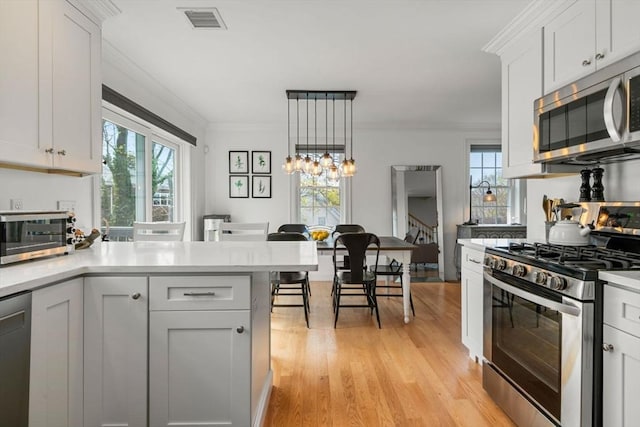 kitchen featuring crown molding, light countertops, light wood-style floors, and appliances with stainless steel finishes