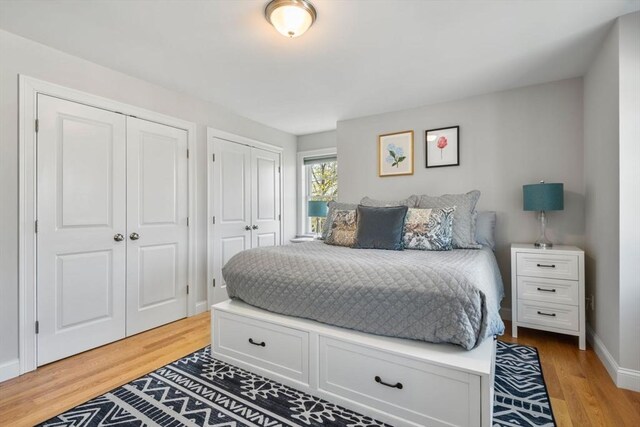 bedroom with baseboards, multiple closets, and light wood finished floors