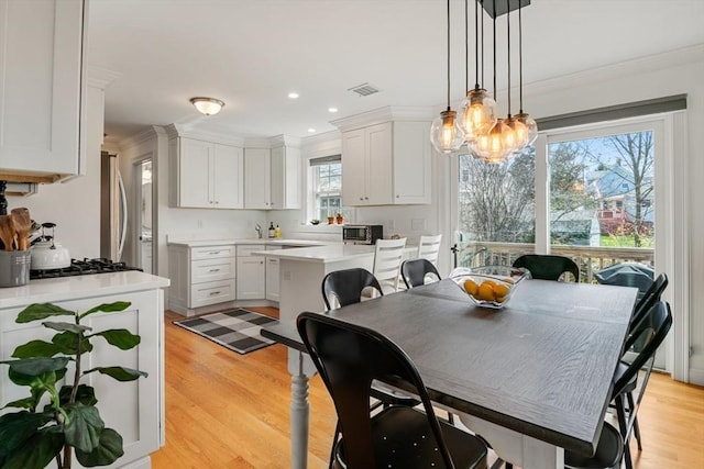 dining space featuring visible vents, ornamental molding, and light wood-style floors