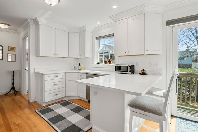 kitchen with a kitchen breakfast bar, a sink, a peninsula, ornamental molding, and white cabinetry