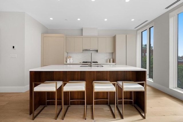 kitchen with a kitchen bar, light wood-type flooring, light countertops, and decorative backsplash