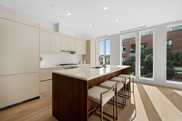 kitchen with a kitchen breakfast bar, backsplash, a sink, and light wood-style floors