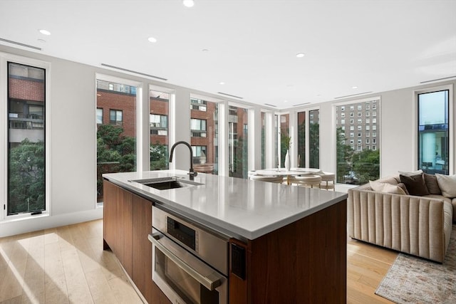 kitchen featuring light wood-type flooring, open floor plan, oven, and a sink