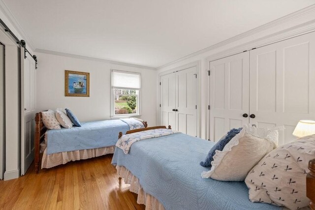 307 Riverview Dr, Chatham, MA 02633 - bedroom featuring a barn door, wood finished floors, multiple closets, and crown molding