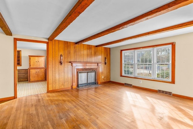 unfurnished living room with light hardwood / wood-style floors, wood walls, beamed ceiling, and a fireplace