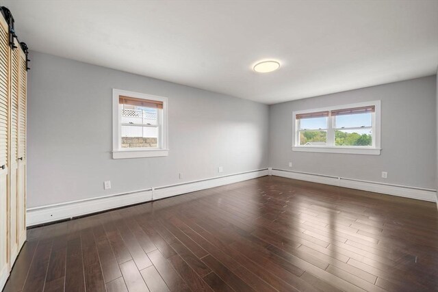152 Audubon Ave, Braintree, MA 02184 - unfurnished bedroom featuring a barn door, baseboards, wood finished floors, and a baseboard radiator