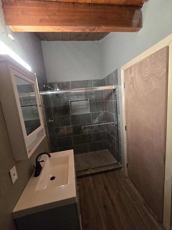 bathroom with a shower with shower door, wood ceiling, wood-type flooring, vanity, and beamed ceiling