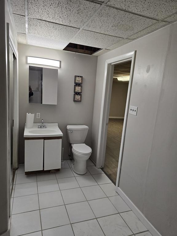 bathroom with a drop ceiling, vanity, tile patterned floors, and toilet