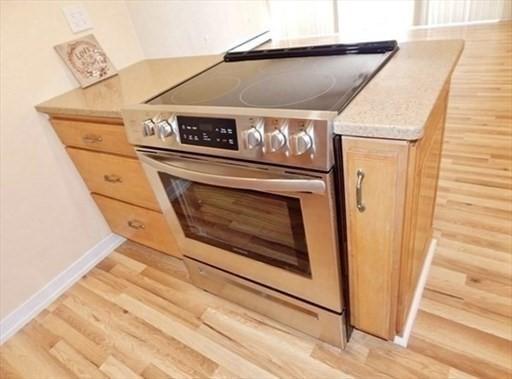 kitchen featuring light wood-type flooring, electric stove, light countertops, and baseboards