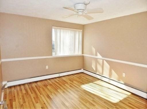 spare room featuring a ceiling fan, baseboard heating, and wood finished floors