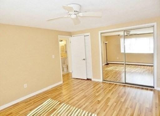 unfurnished bedroom with a baseboard radiator, wood finished floors, two closets, and baseboards