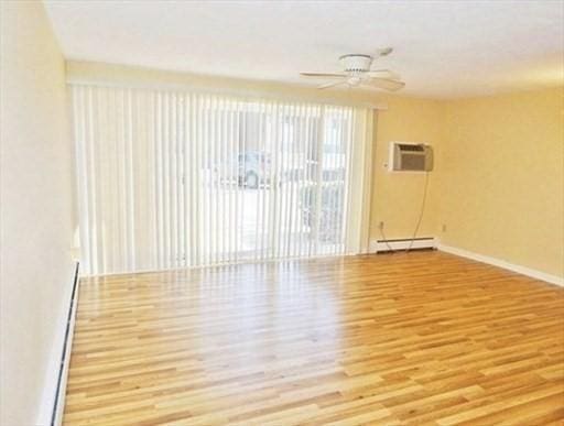 empty room featuring a ceiling fan, a baseboard radiator, a wall mounted air conditioner, and wood finished floors