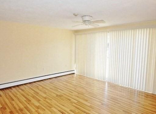 empty room featuring a ceiling fan, a baseboard heating unit, and wood finished floors