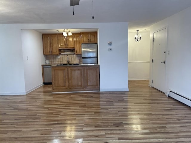 kitchen with tasteful backsplash, baseboards, appliances with stainless steel finishes, brown cabinets, and wood finished floors