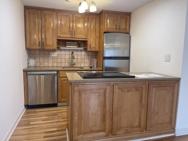 kitchen featuring light wood finished floors, decorative backsplash, brown cabinetry, stainless steel appliances, and a sink