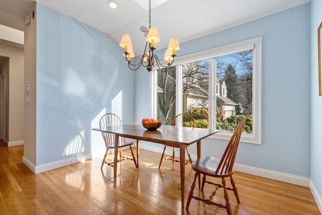 dining space featuring vaulted ceiling, a notable chandelier, and light hardwood / wood-style flooring