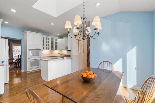 dining room featuring sink, light hardwood / wood-style flooring, a chandelier, and vaulted ceiling