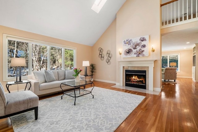 living room with a skylight, plenty of natural light, a tiled fireplace, and wood-type flooring