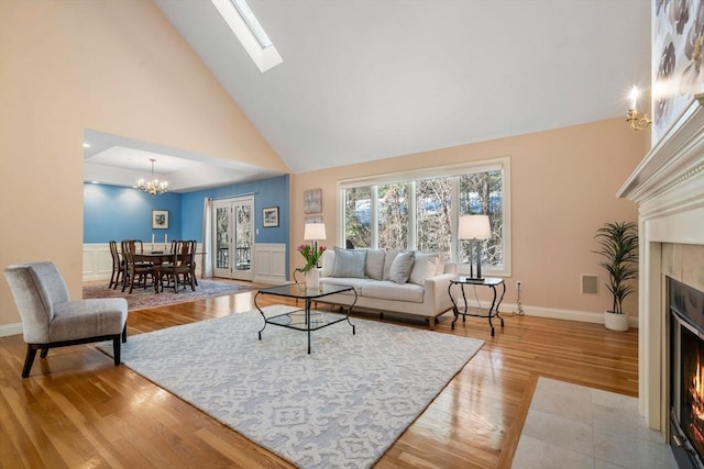 living room with high vaulted ceiling, a notable chandelier, light hardwood / wood-style floors, and a skylight