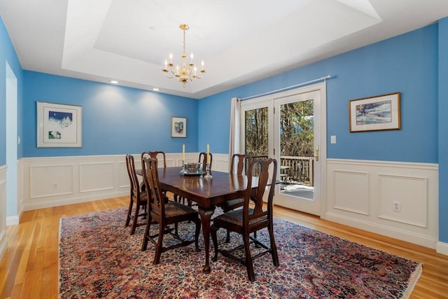 dining area with a tray ceiling, light hardwood / wood-style flooring, and a notable chandelier