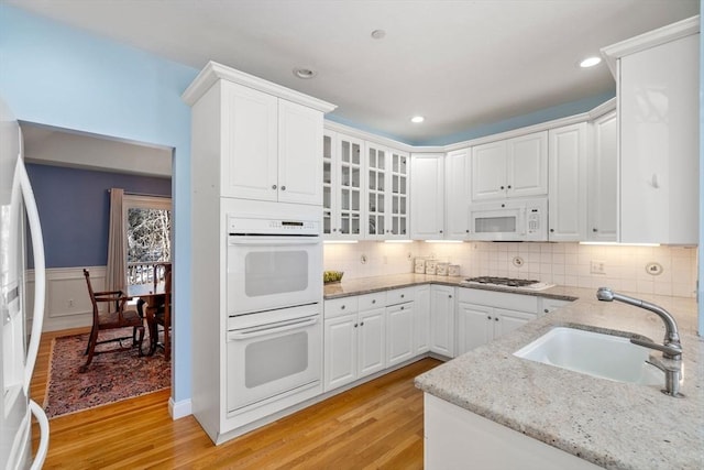 kitchen with sink, light stone counters, light wood-type flooring, white appliances, and white cabinets