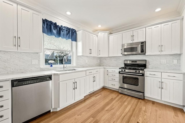 kitchen with light wood finished floors, appliances with stainless steel finishes, ornamental molding, white cabinetry, and a sink