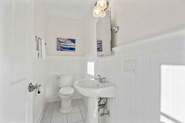 half bathroom featuring toilet, tile patterned floors, crown molding, and wainscoting