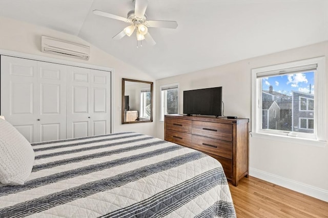 bedroom with lofted ceiling, a wall unit AC, light wood-style flooring, multiple windows, and a closet