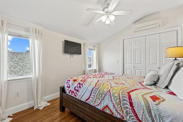 bedroom featuring lofted ceiling, a closet, an AC wall unit, wood finished floors, and baseboards