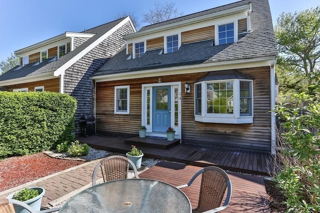 view of front of house with a deck, outdoor dining space, and a shingled roof