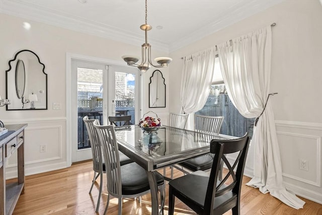 dining room featuring ornamental molding, wainscoting, light wood-style flooring, and a decorative wall