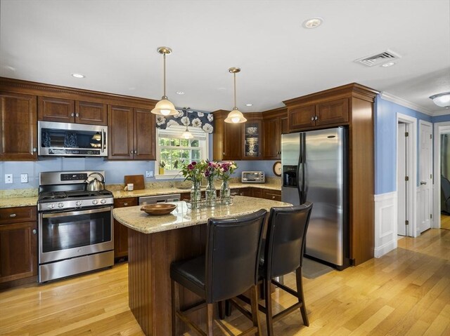10 Robinhood Rd, Tyngsborough, MA 01879 - kitchen featuring stainless steel appliances, light wood finished floors, light stone counters, ornamental molding, and a wainscoted wall