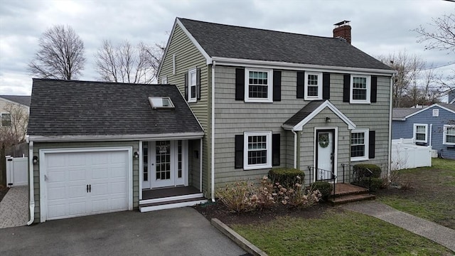 colonial home featuring a chimney, an attached garage, driveway, and a shingled roof