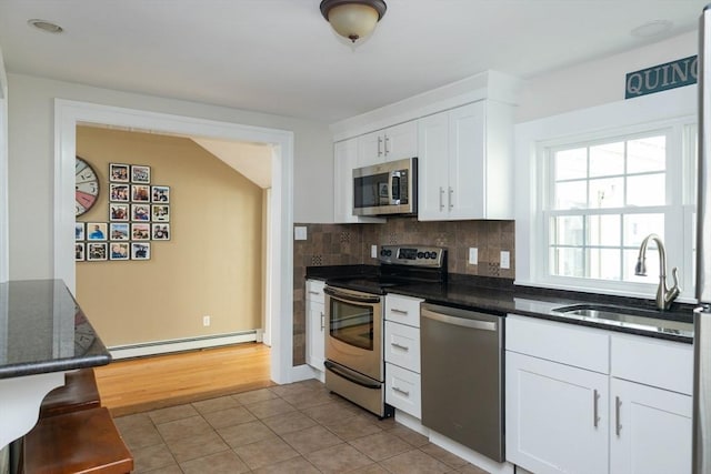 kitchen with a sink, white cabinetry, baseboard heating, appliances with stainless steel finishes, and light tile patterned floors