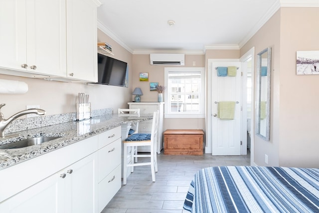 kitchen featuring a wall mounted air conditioner, ornamental molding, white cabinetry, sink, and light stone countertops