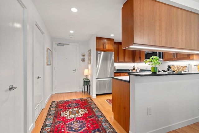 80 Broad St Unit 1002, Boston, MA 02110 - kitchen with brown cabinets, dark countertops, stainless steel appliances, light wood-style floors, and recessed lighting