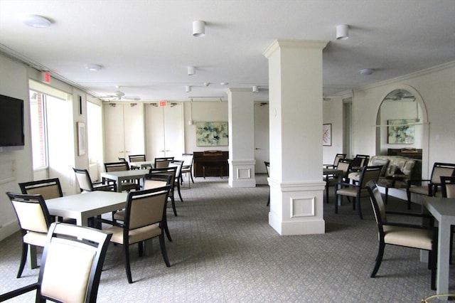 carpeted dining area featuring crown molding, decorative columns, ceiling fan, and a decorative wall