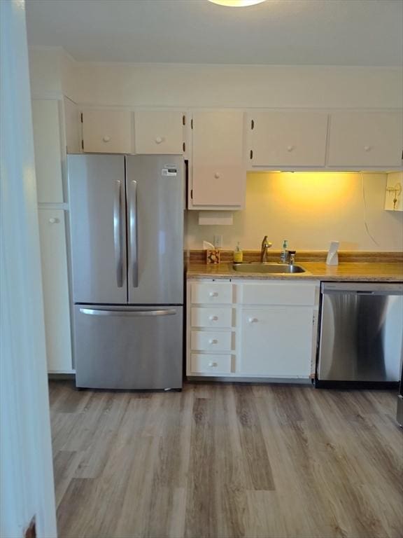 kitchen with light wood-type flooring, light countertops, white cabinetry, a sink, and appliances with stainless steel finishes