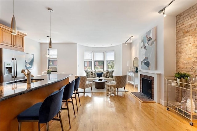 kitchen with fridge with ice dispenser, a fireplace, a sink, light wood-style floors, and a kitchen breakfast bar