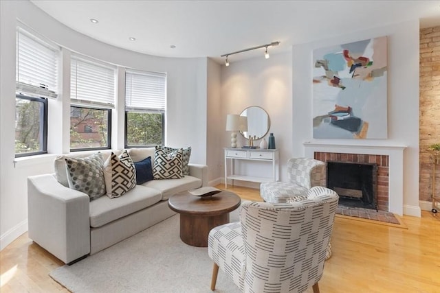 living area featuring track lighting, a brick fireplace, baseboards, and light wood-style floors